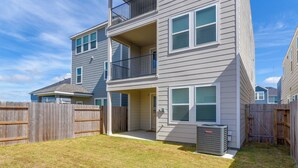 A two-story residential building with a balcony, a fenced yard, and a visible air conditioning unit.