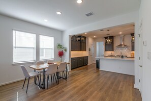 A modern kitchen with dark cabinets, a central island, and a dining area with a wooden table and chairs.