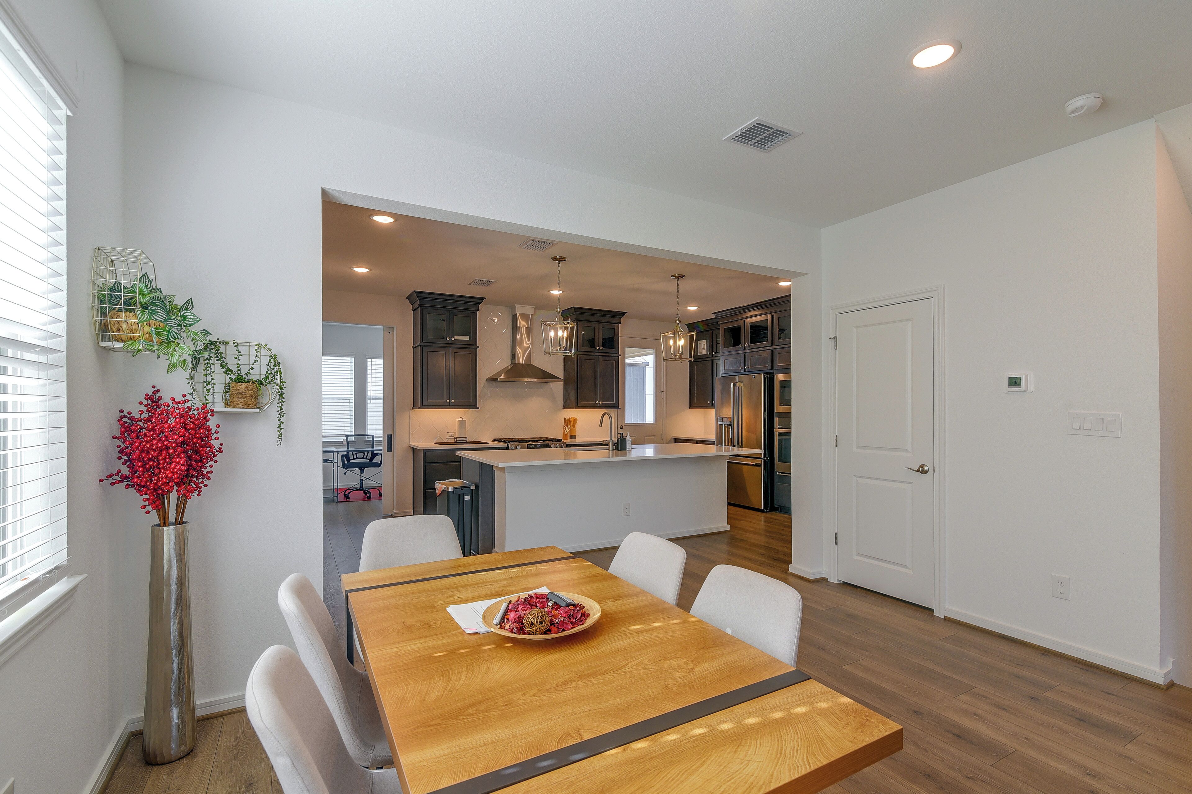 A modern kitchen with dark cabinetry, a central island, and a dining area with a wooden table and white chairs.