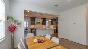 A modern kitchen with dark cabinetry, a central island, and a dining area with a wooden table and white chairs.