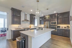 A modern kitchen with dark cabinetry, a large island, stainless steel appliances, and pendant lighting.