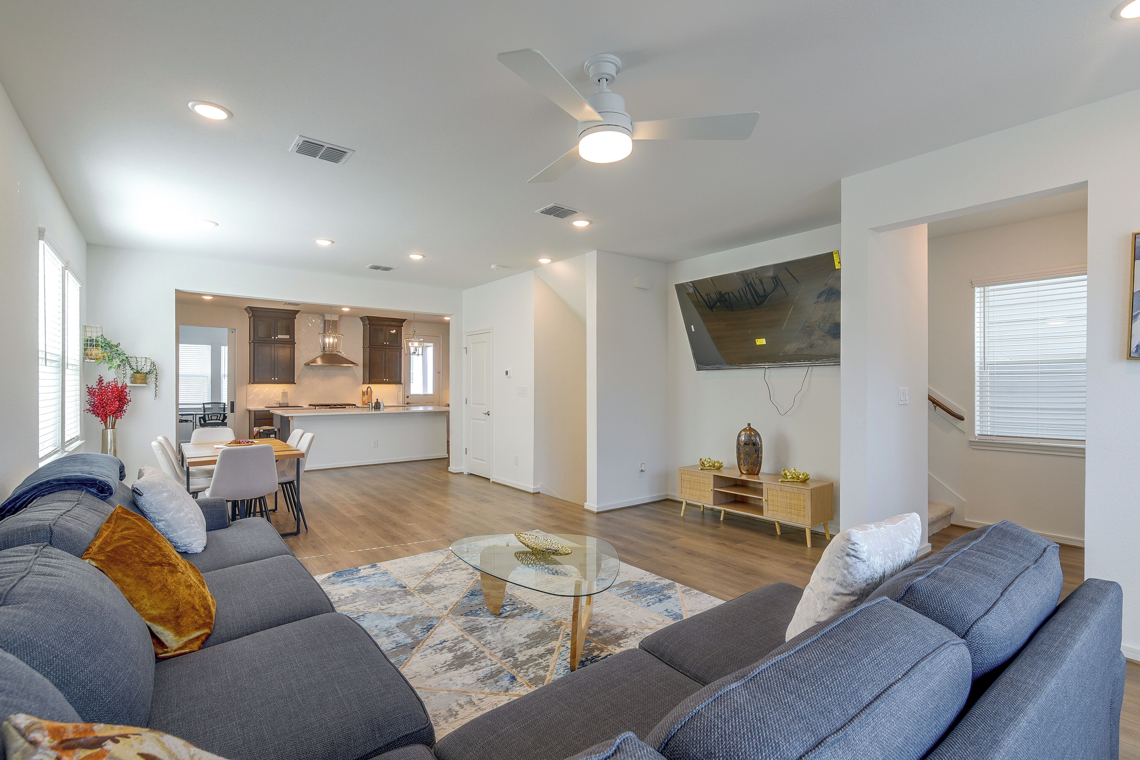 A modern living room with a gray sofa, a glass coffee table, and a kitchen in the background.