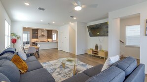 A modern living room with a gray sofa, a glass coffee table, and a kitchen in the background.