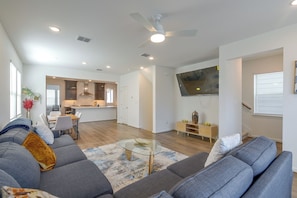 A modern living room with a gray sofa, a glass coffee table, and a kitchen in the background.