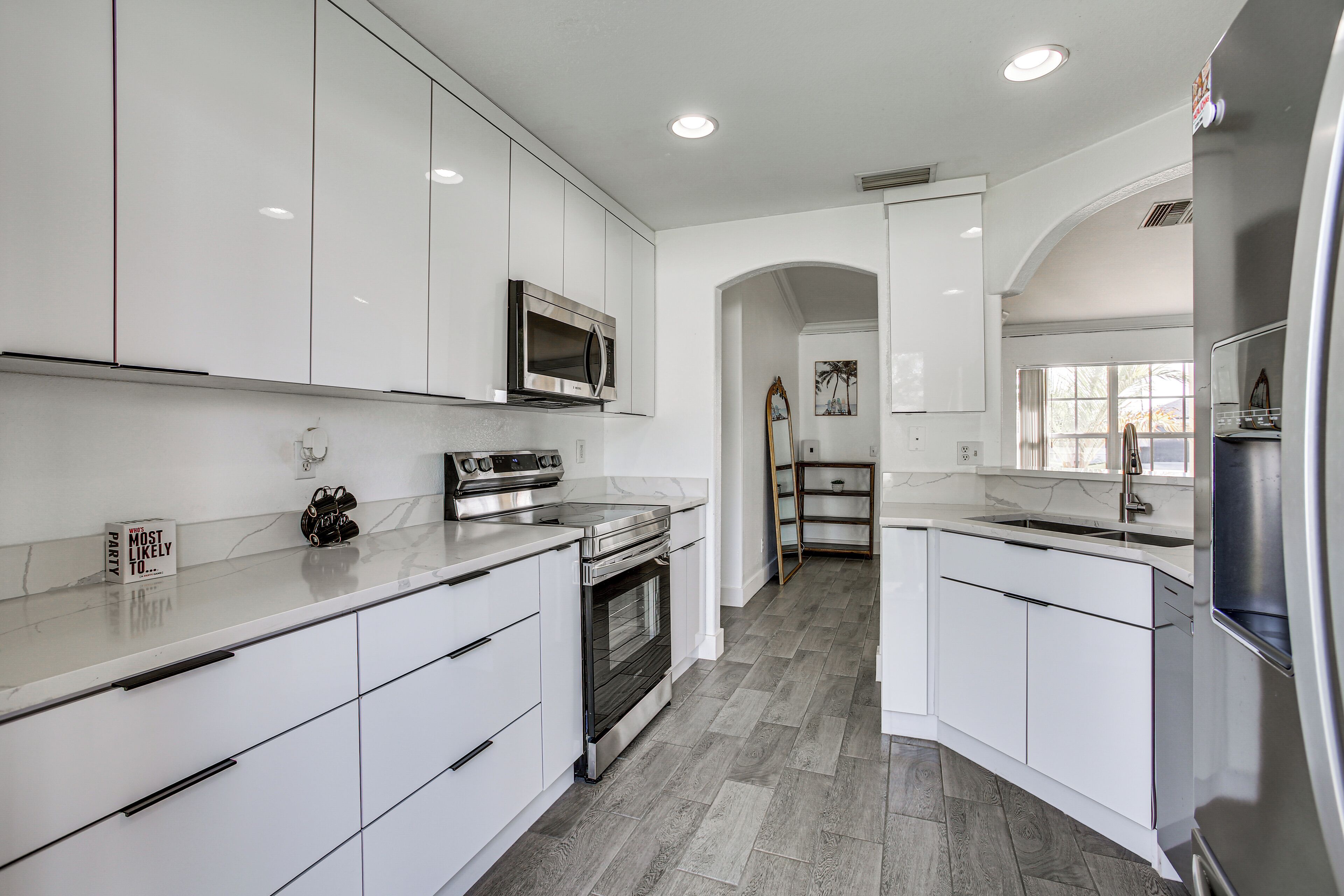 A modern kitchen with white cabinetry, stainless steel appliances, and a herringbone-patterned floor.