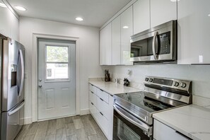 A modern kitchen with stainless steel appliances, white cabinetry, and a window. - Bright Cape Coral Home, 9 Mi to Downtown (Cape Coral)