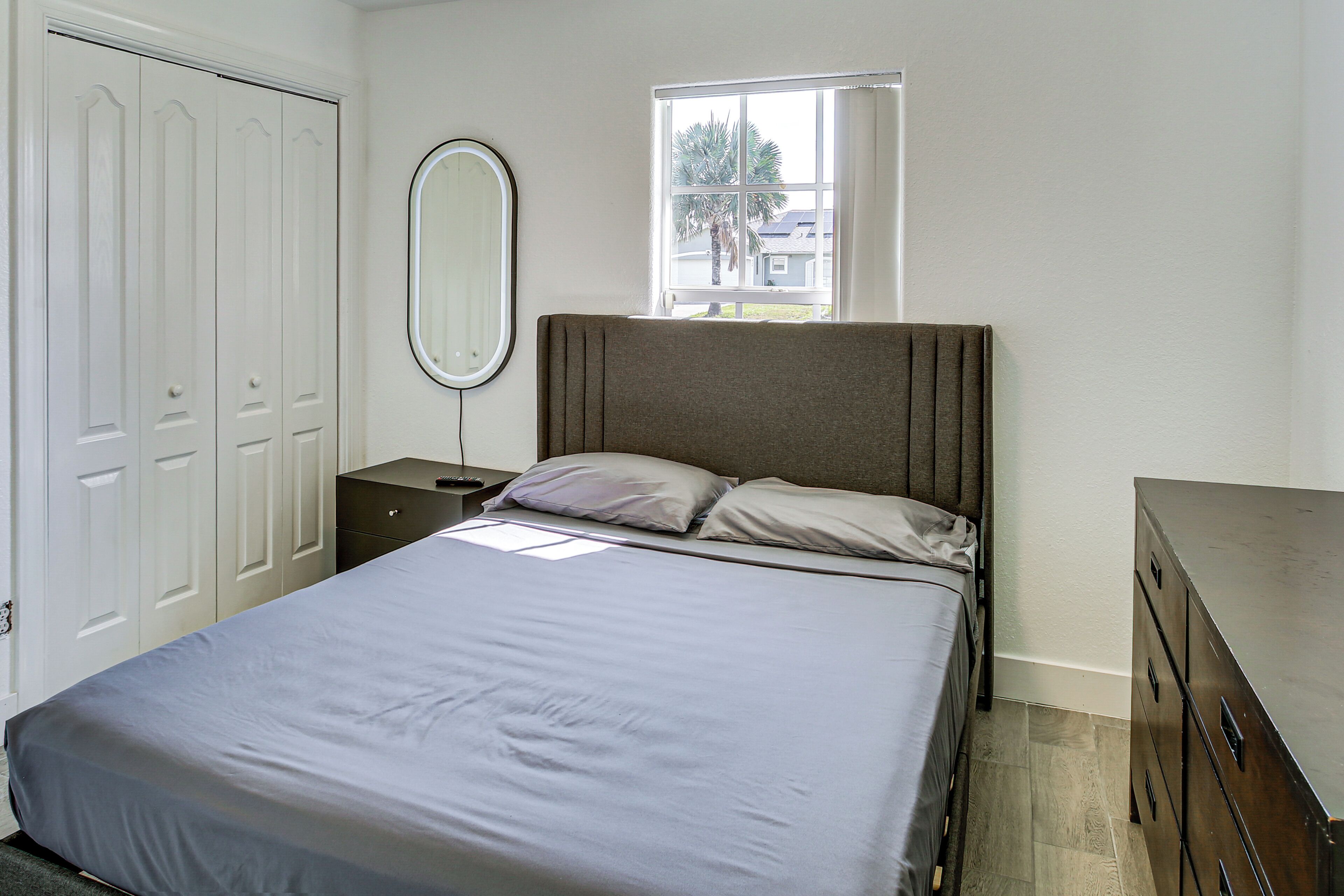 A bedroom with a bed, a nightstand, a dresser, a mirror, and a window.