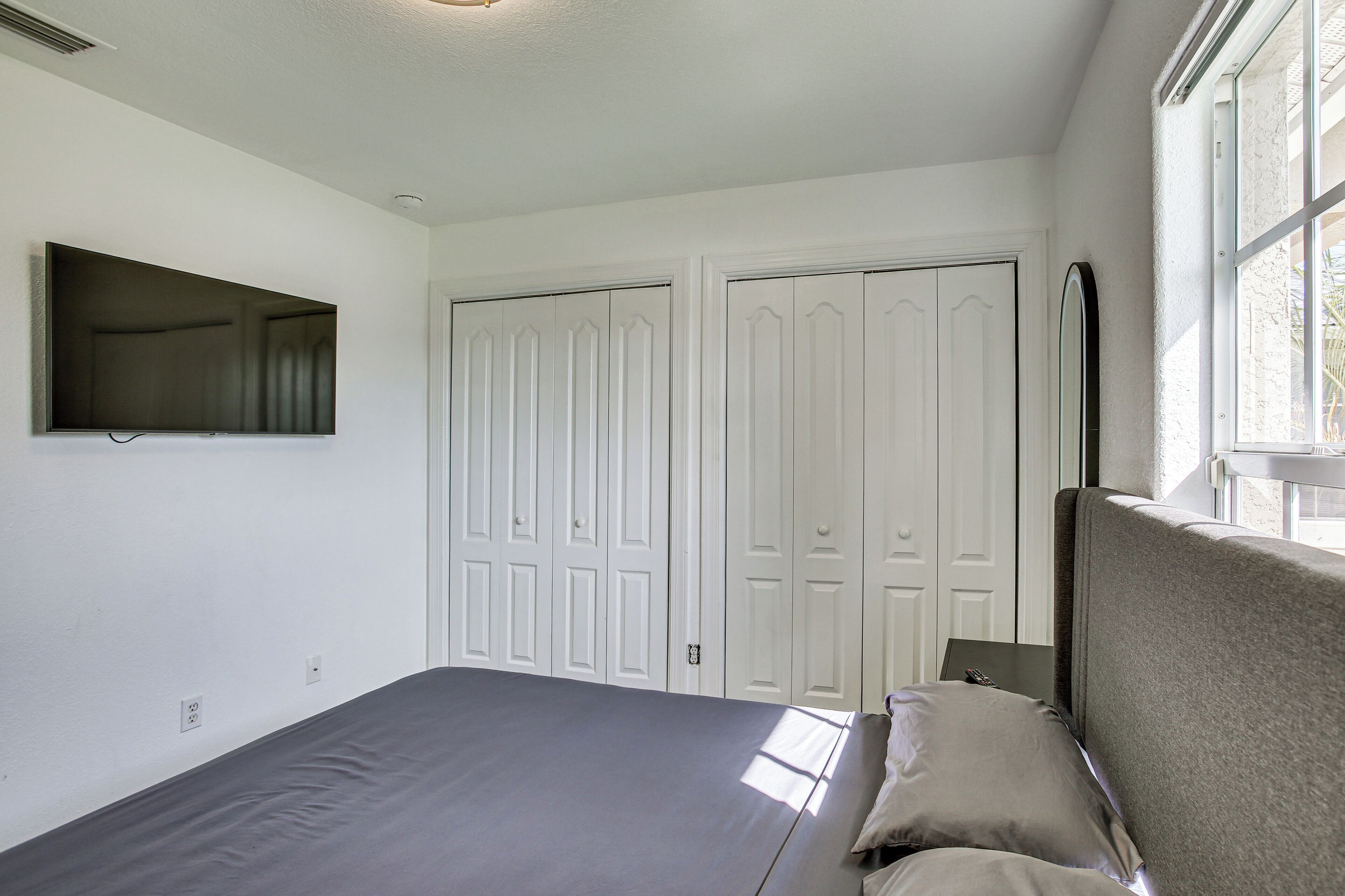 Une chambre à coucher avec un lit, un téléviseur fixé au mur et une fenêtre.