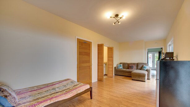 Habitación amplia con cama, sofá y refrigerador. Cuenta con puertas de madera y una lámpara en el techo.