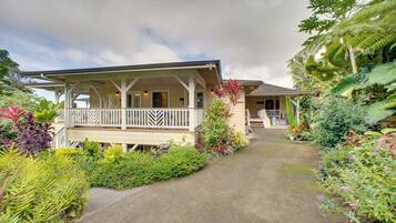 A two-story house with a porch, surrounded by lush tropical plants.
