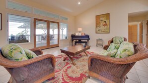 Un salón espacioso con mobiliario de mimbre, un piano y un amplio ventanal.