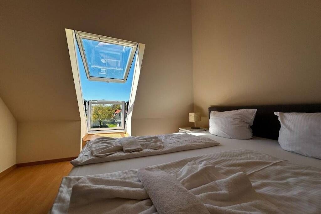 Quarto com claraboia, uma cama com almofadas e uma mesa de cabeceira.