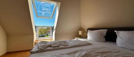 Quarto com claraboia, uma cama com almofadas e uma mesa de cabeceira.