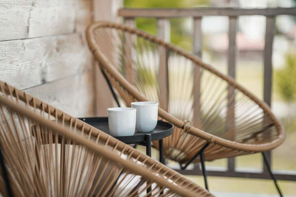 Wicker chairs and a small table with two white cups on a balcony.