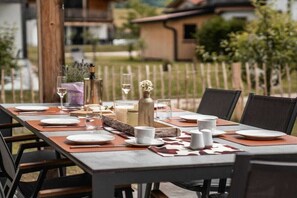 An outdoor dining area with a long table set for a meal, surrounded by chairs.