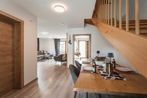 Un interior modern amb una escala de fusta, una zona de menjador amb taula per a dues persones, i un saló al fons.