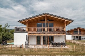 A two-story wooden cabin with a balcony, a barbecue grill, and a patio area with outdoor seating.