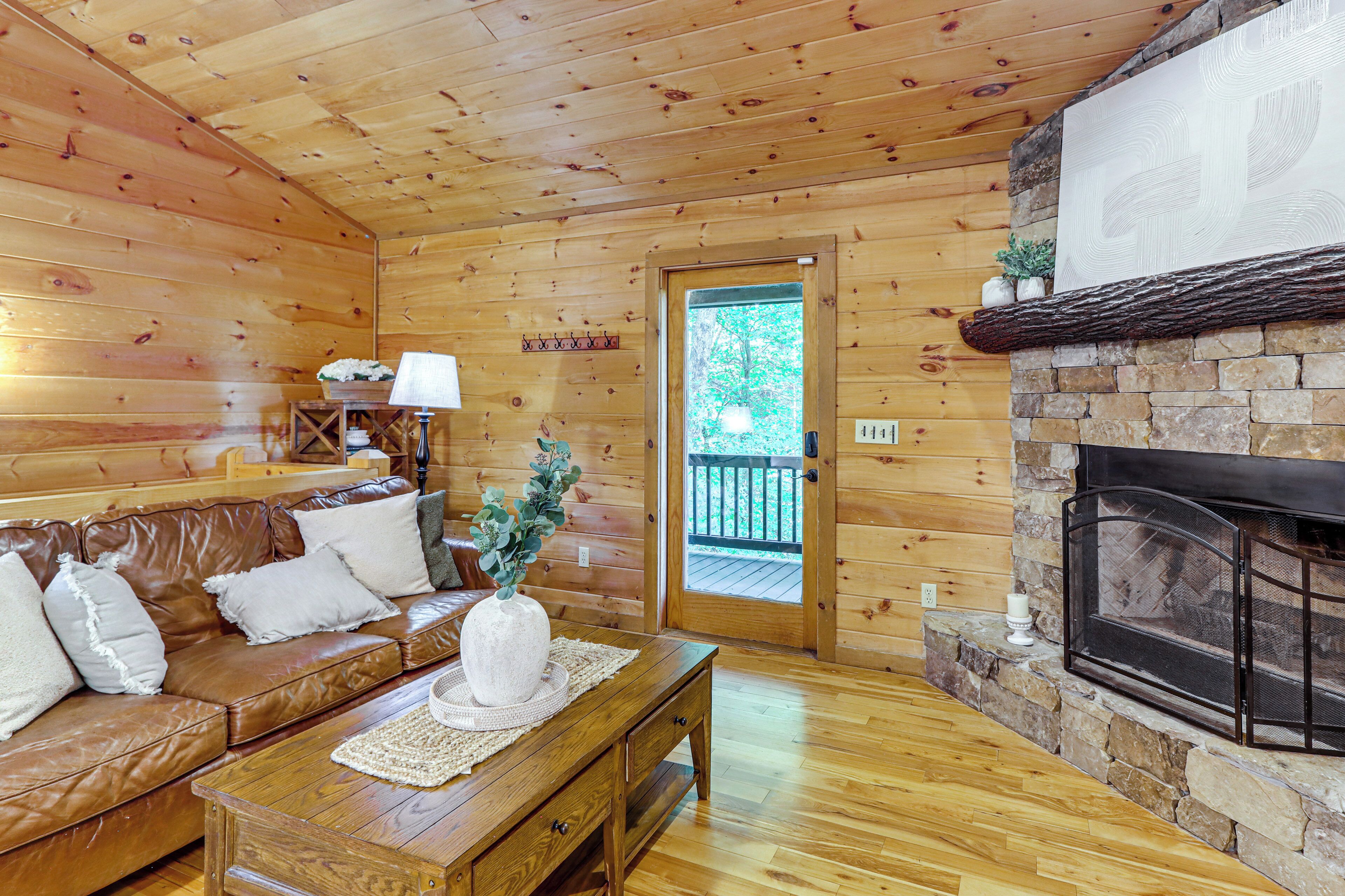 A wooden interior with a leather sofa, a stone fireplace, and a door leading outside.