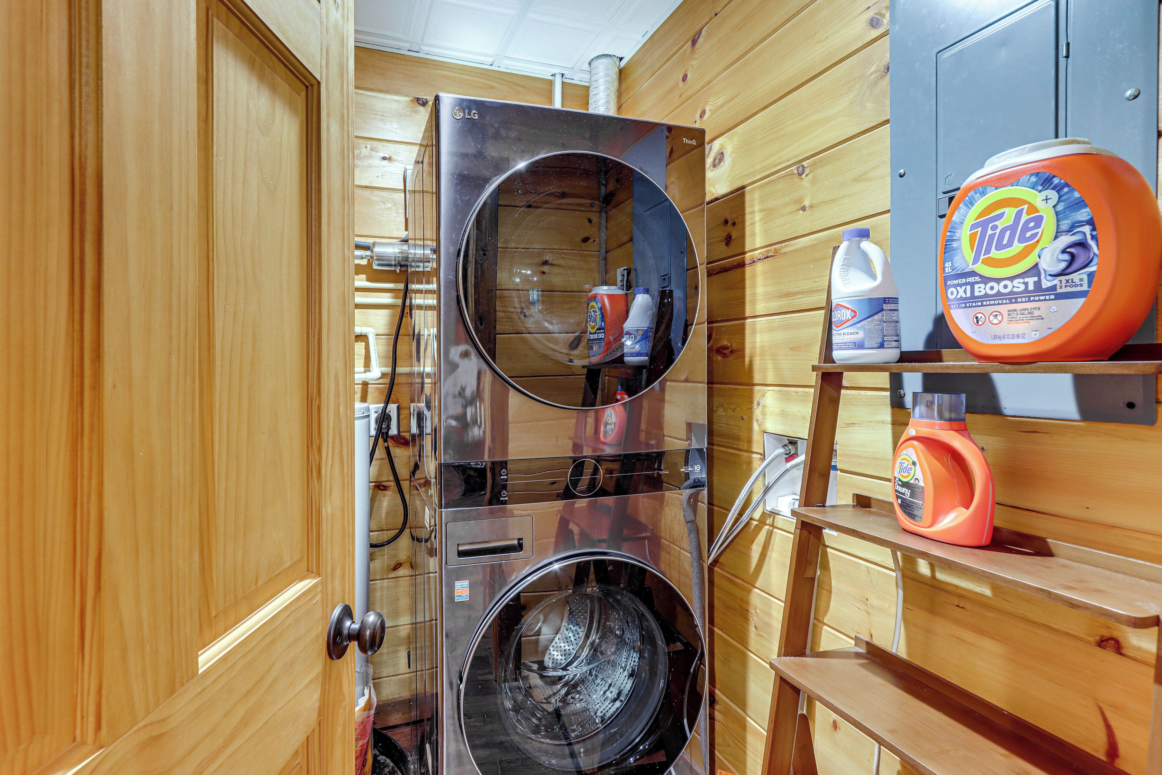 A compact laundry area with a washing machine and dryer, a shelf with laundry detergent, and a door leading to another room.