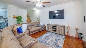 A living room with a sectional sofa, a flat-screen TV, a ceiling fan, and a wooden entertainment center. - Home Gym & Pool Access! North Raleigh Retreat (Raleigh)