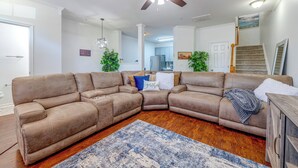 A spacious living room with a large sectional sofa, a ceiling fan, and a kitchen in the background. - Home Gym & Pool Access! North Raleigh Retreat (Raleigh)