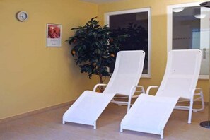 Una habitación con tres sillones blancos, una planta en maceta, un cuadro en la pared y una ventana.