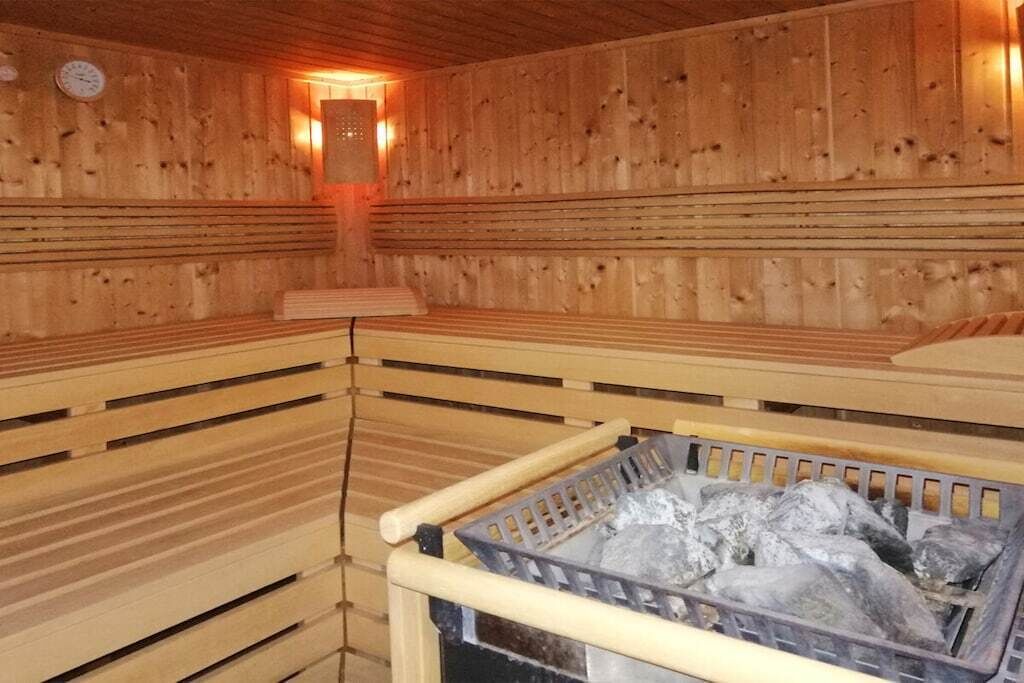 A sauna with wooden walls, benches, and a basket of stones.