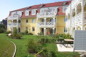 Ein mehrstöckiges Gebäude mit Balkonen, einem roten Ziegeldach und einem gepflegten Garten.