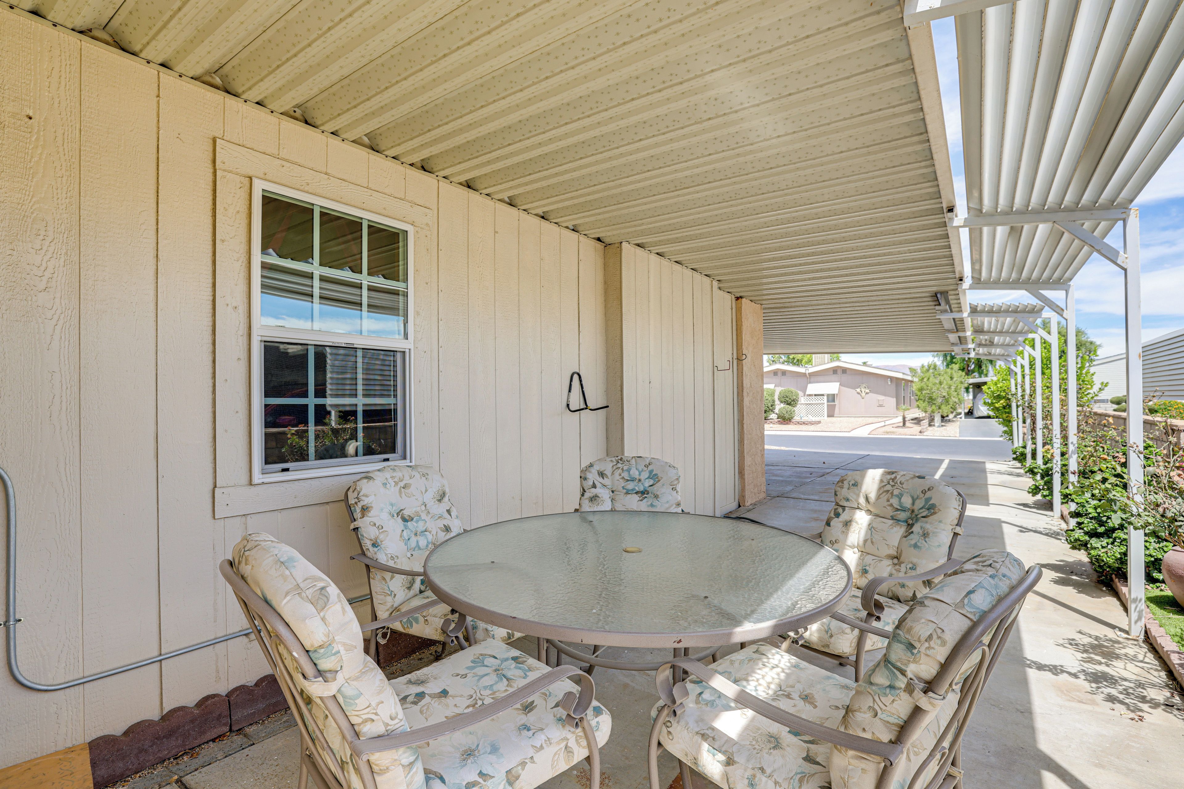 A covered patio with a round table and floral chairs, a window, and a metal railing.