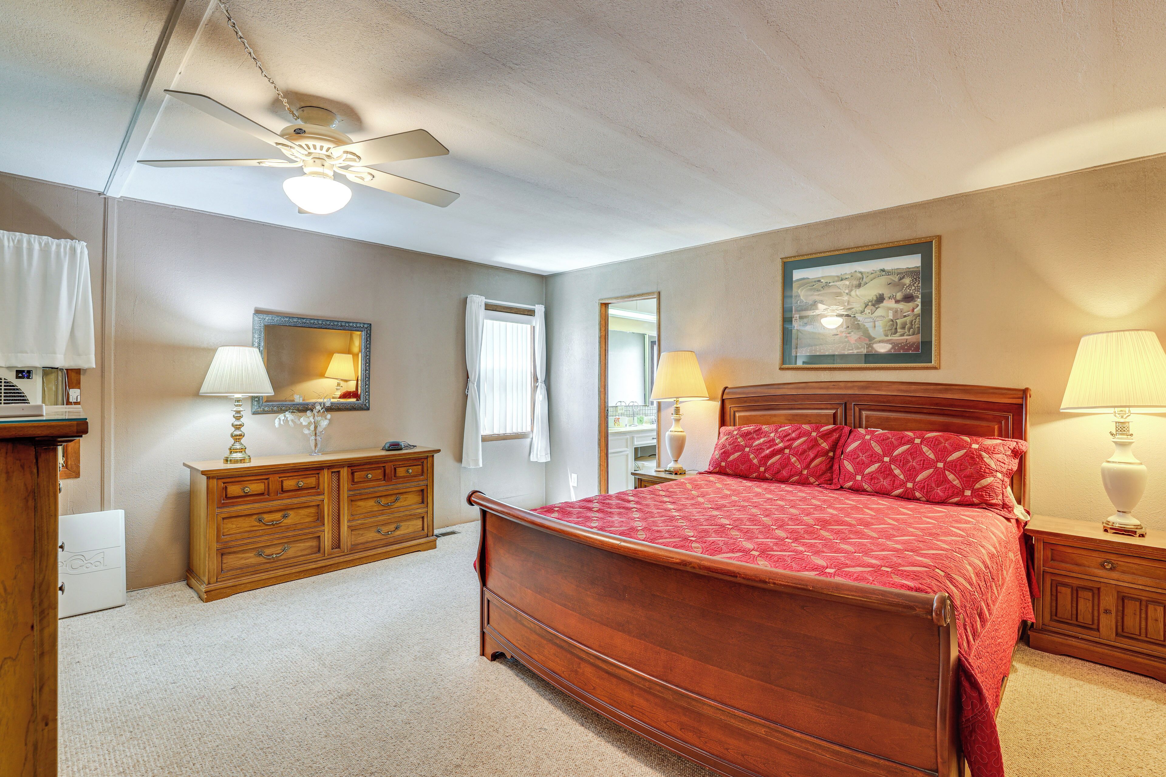 A bedroom with a wooden bed, a ceiling fan, a dresser, and a painting on the wall.