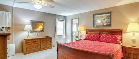 A bedroom with a wooden bed, a ceiling fan, a dresser, and a painting on the wall.