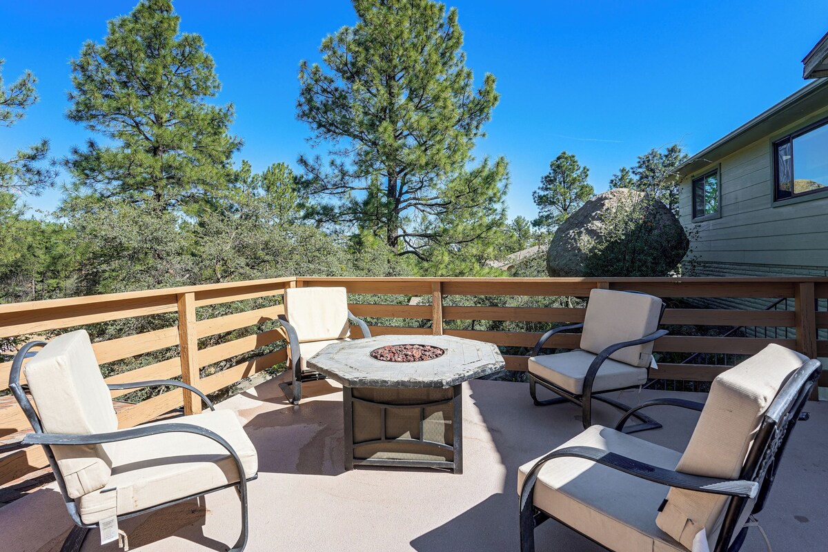 A patio with outdoor seating, a fire pit, and a view of surrounding trees and a house.