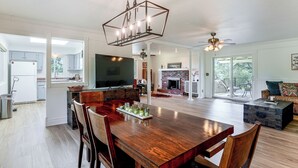 Uma sala de estar espaçosa com uma mesa de jantar de madeira, cadeiras, lareira e televisão.