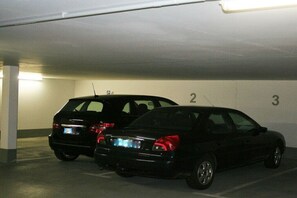 Zwei Autos stehen in einer schlecht beleuchteten Tiefgarage mit nummerierten Stellplätzen.