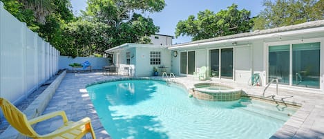A swimming pool with a hot tub, surrounded by a patio with chairs and a fence.