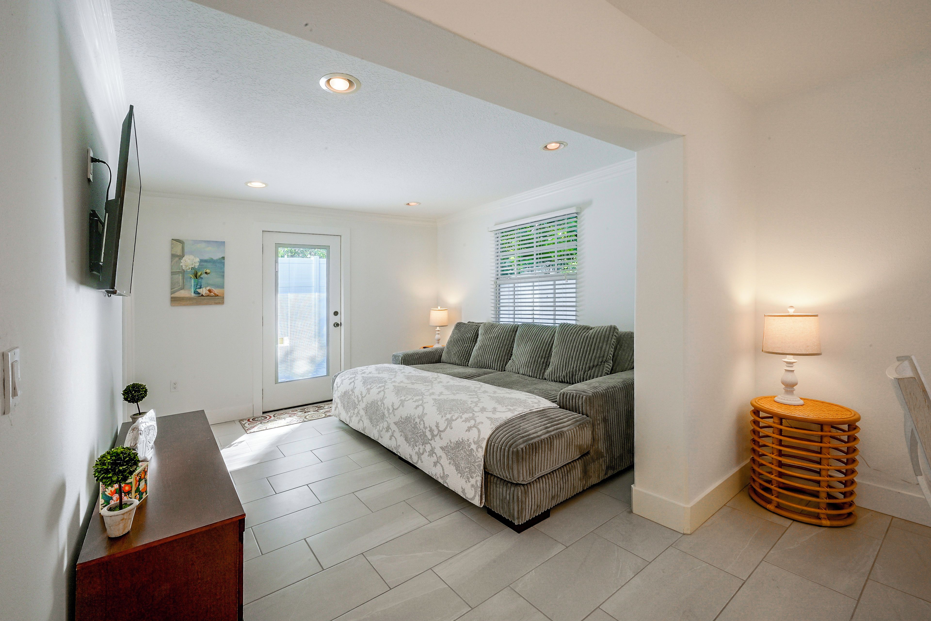A bedroom with a bed, a bedside table, a lamp, a window with blinds, and a door.