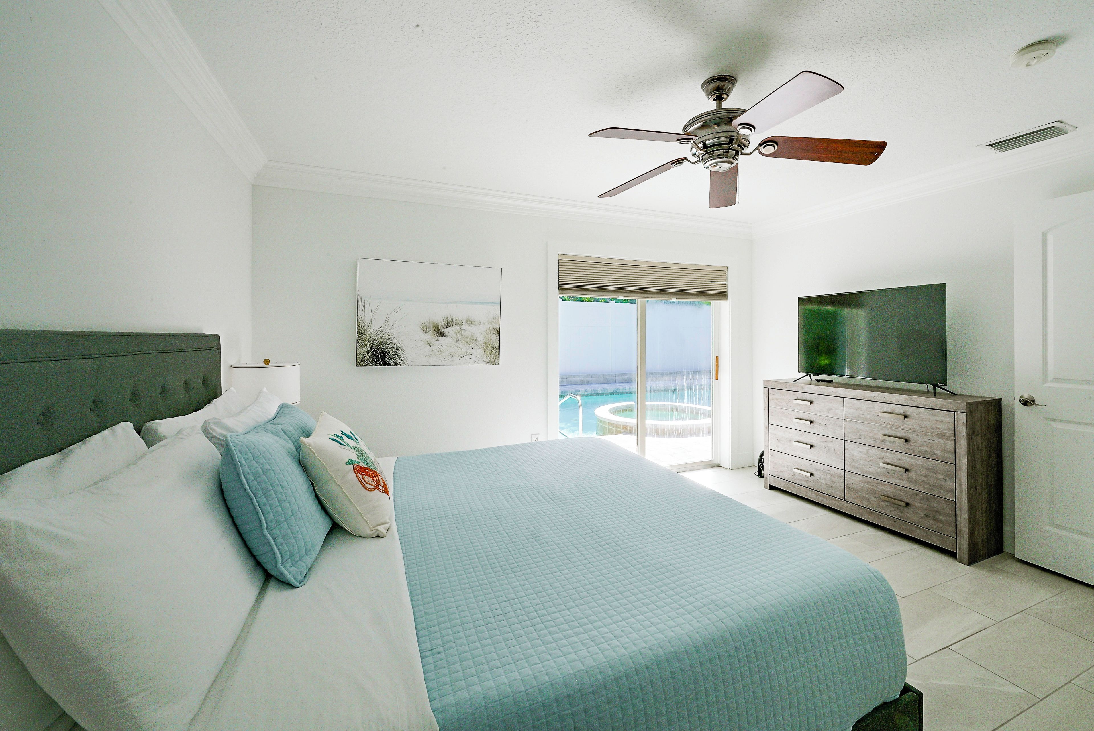 A bedroom with a bed, a dresser, a television, and a ceiling fan.