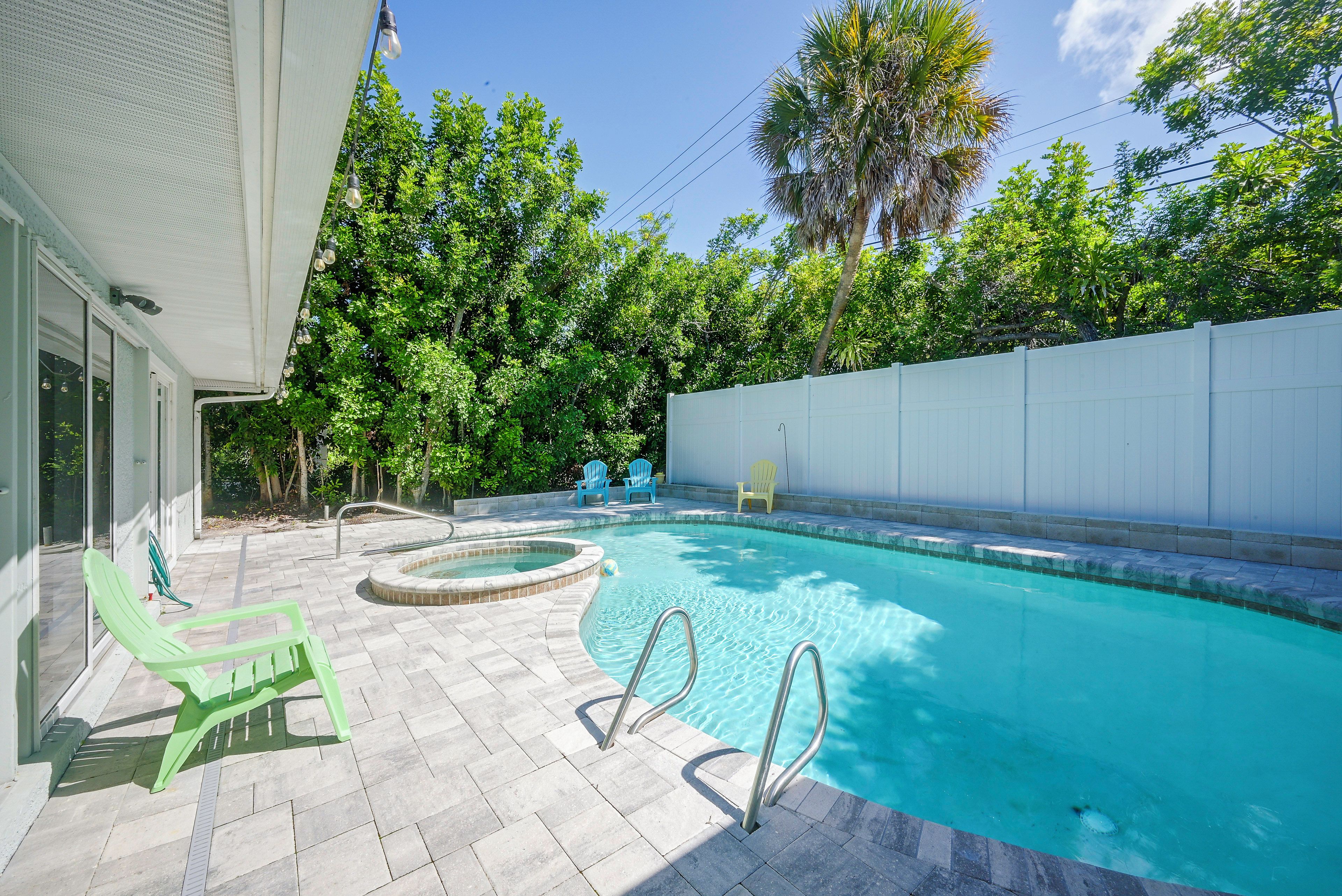 A swimming pool with a hot tub, surrounded by a white fence, and a patio area with chairs.