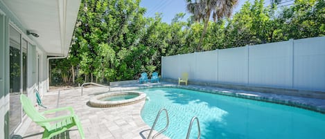 A swimming pool with a hot tub, surrounded by a white fence, and a patio area with chairs.