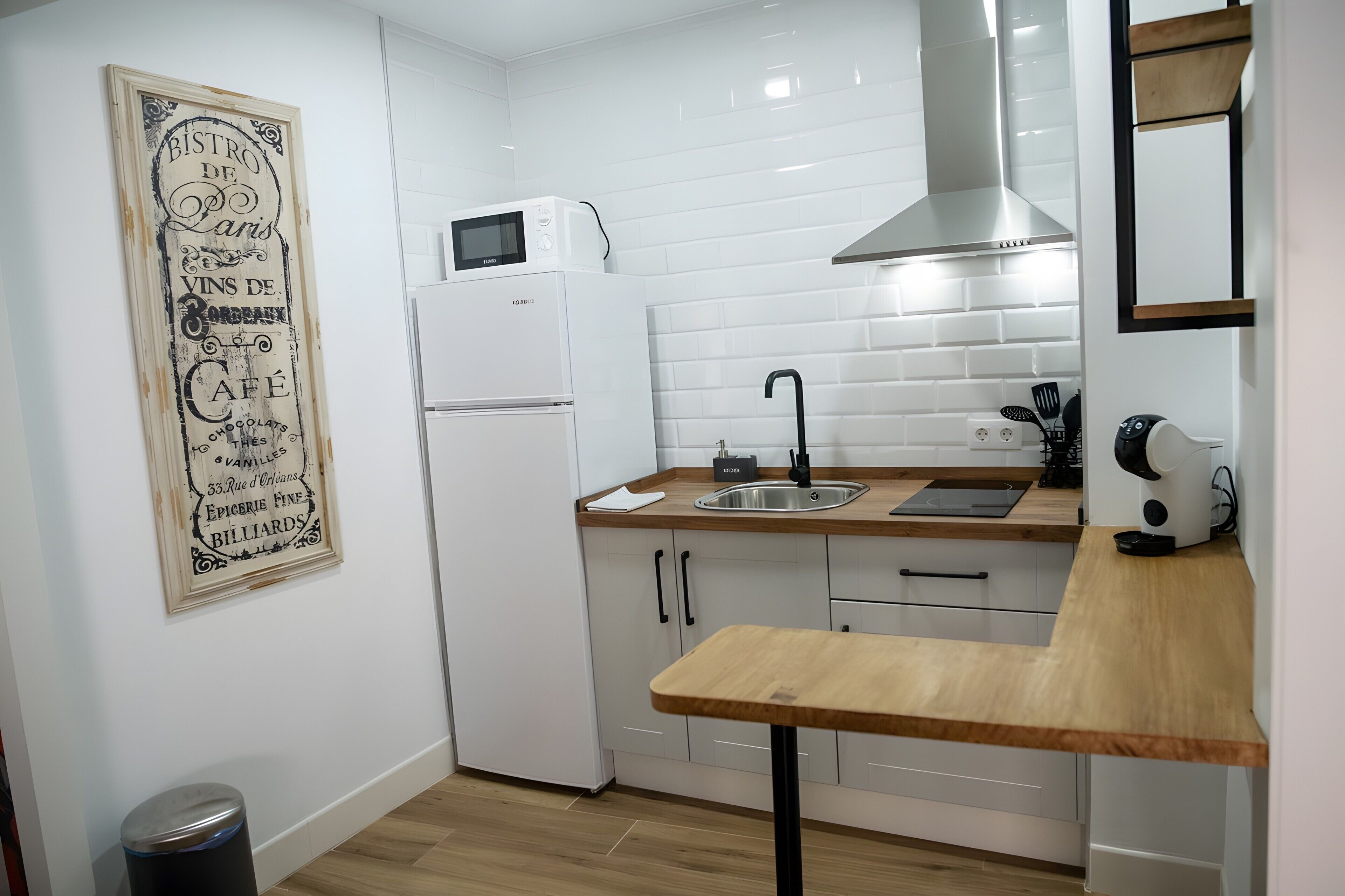 Eine kompakte Küche mit weißen Schränken, einer integrierten Mikrowelle, einem Edelstahl-Spülbecken und einer Holz Arbeitsplatte.