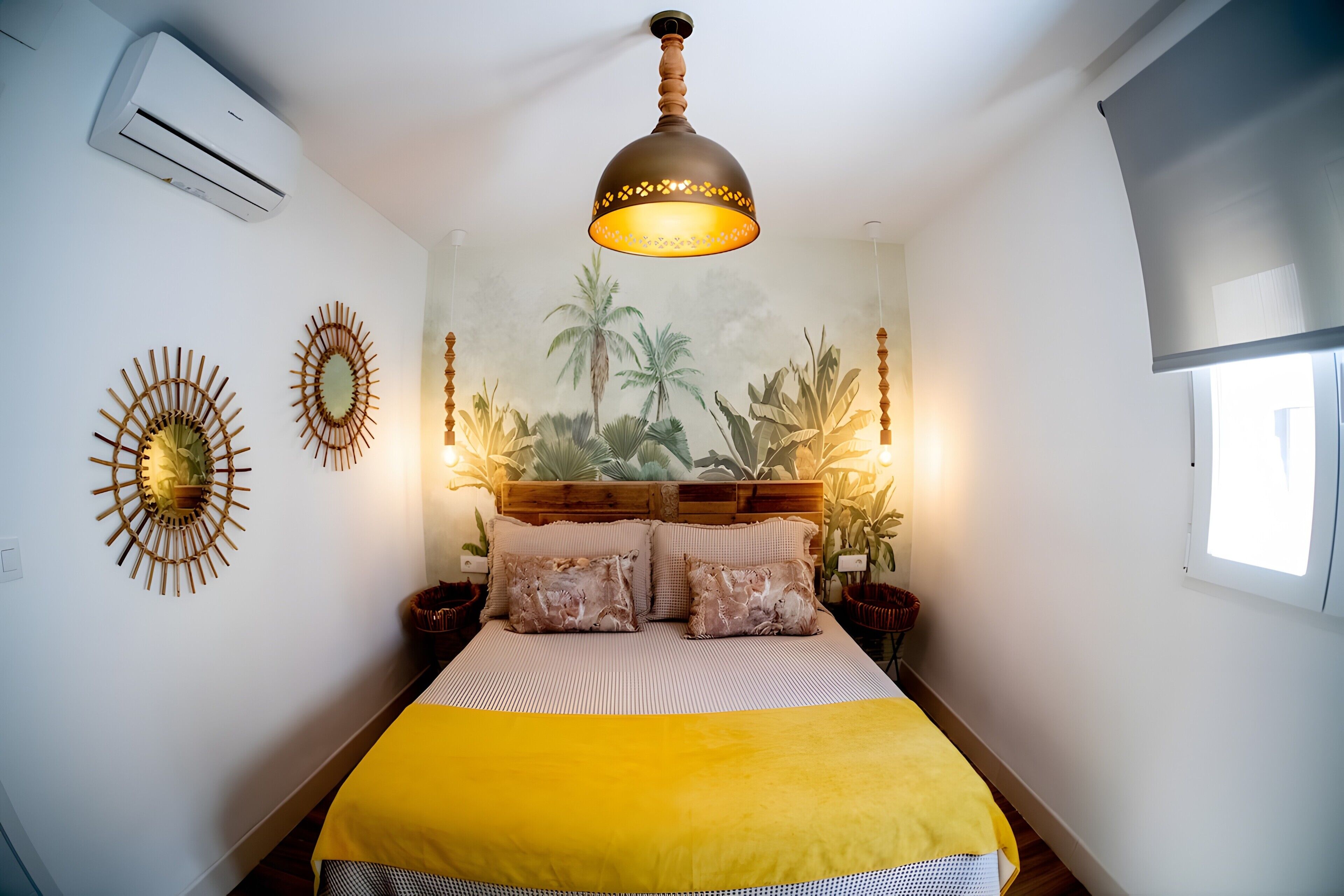 A bedroom with a bed, a wall-mounted air conditioner, a decorative ceiling light, and a mural of tropical plants.
