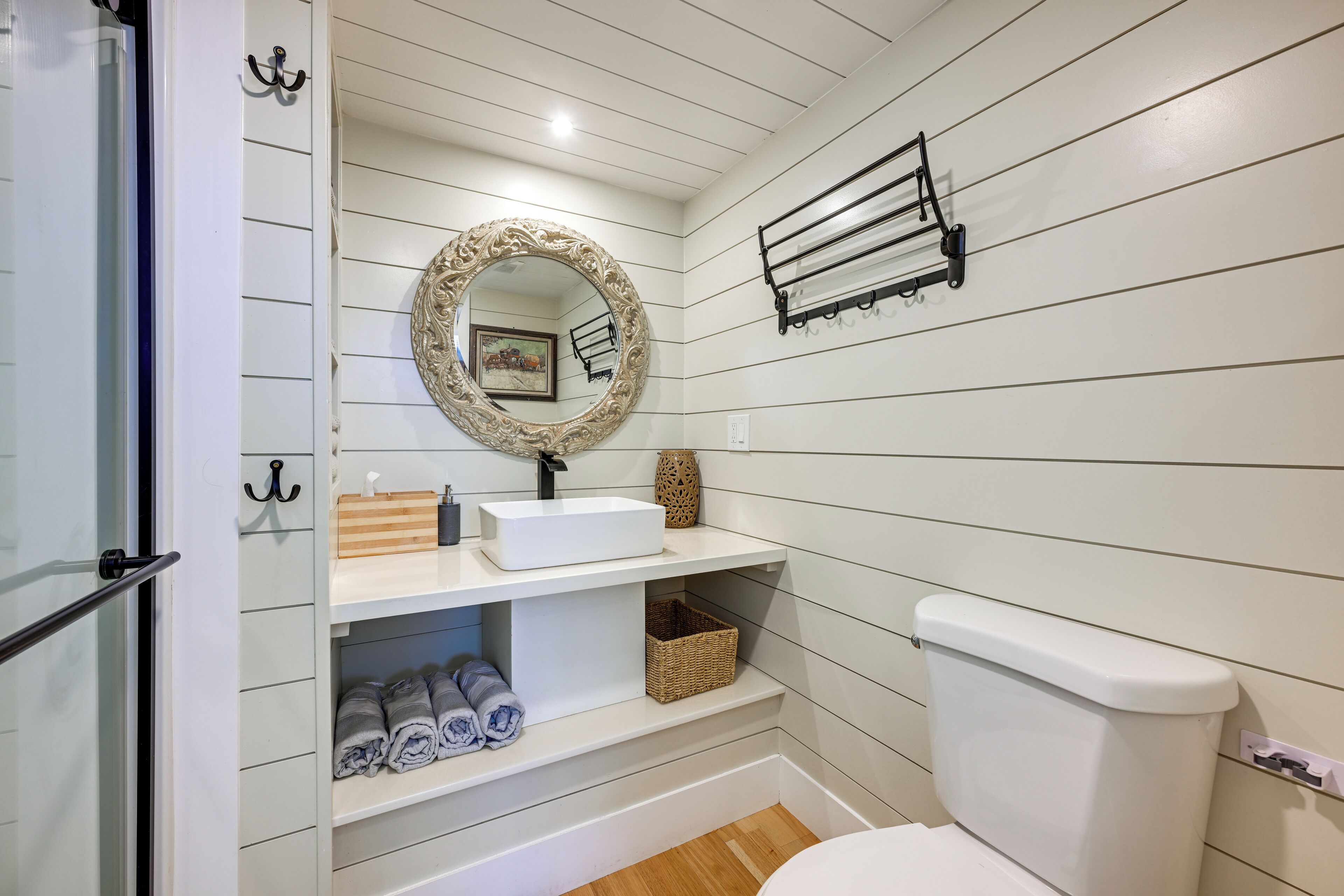 A bathroom with a white sink, a mirror with an ornate frame, a towel rack, and a toilet.