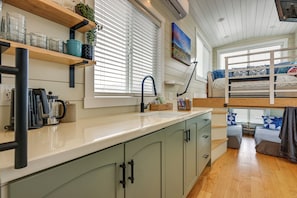A compact kitchen with a sink, a coffee maker, and a window with blinds.