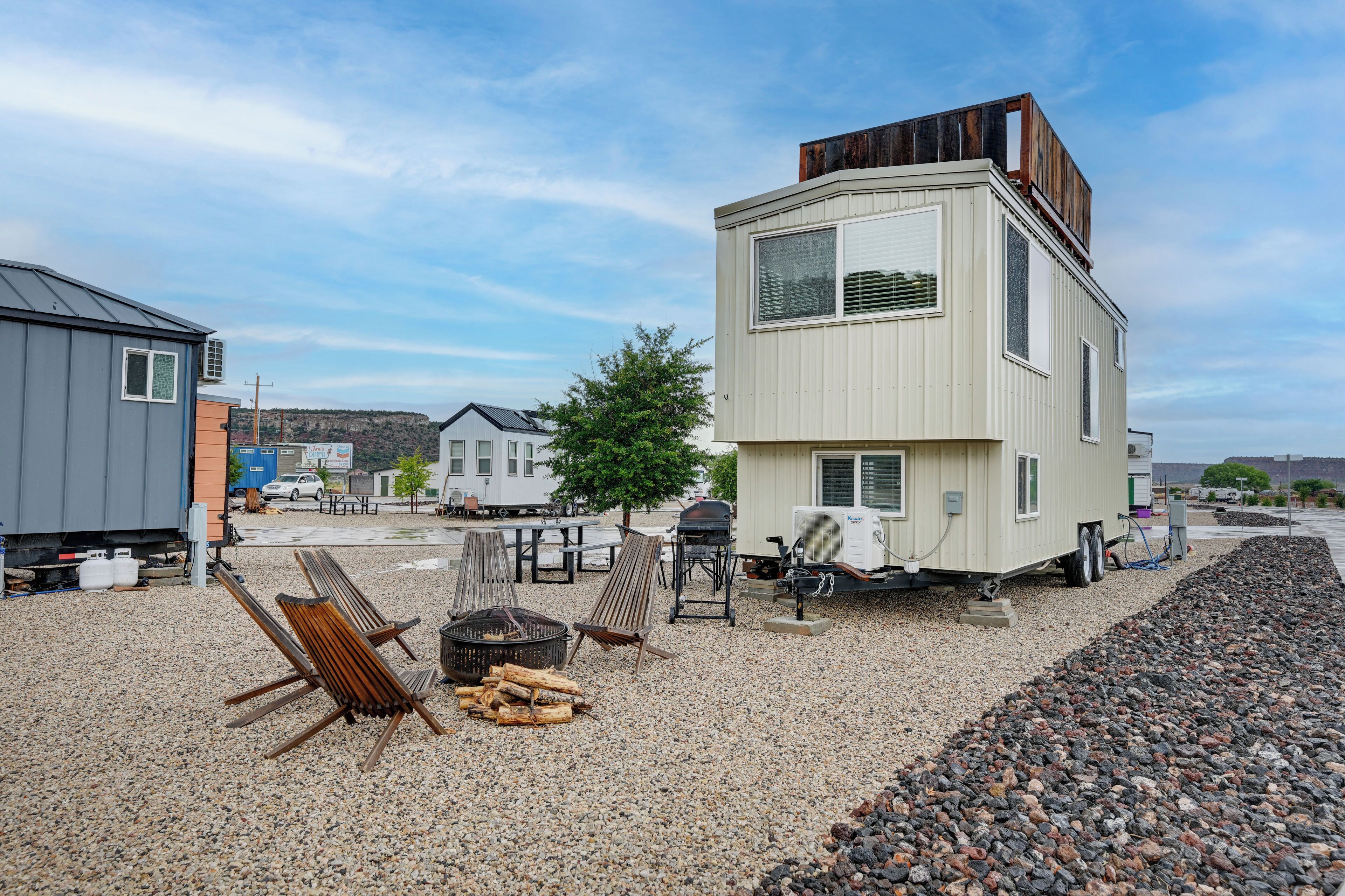 Ein moderner Wohnmobilwagen mit weißer Außenfarbe und einer Holzterrasse, ausgestattet mit Grill und Sitzgelegenheiten.