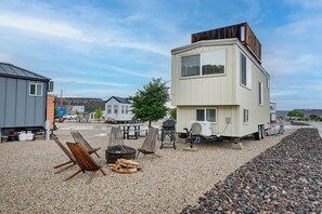 A modern RV with a white exterior and a wooden deck area, equipped with a grill and seating.