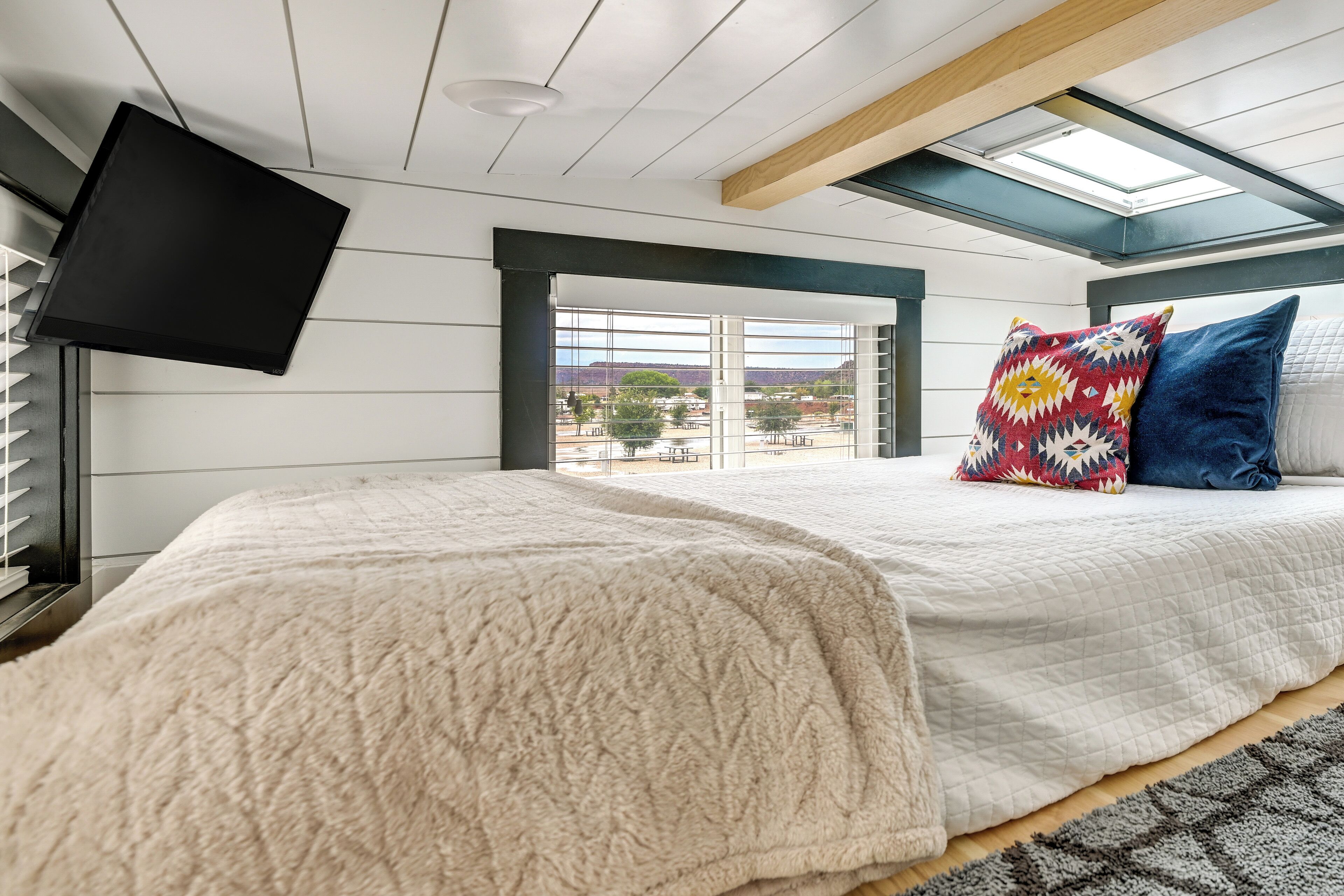 Un dormitorio con cama, televisor, tragaluz y vistas al exterior.