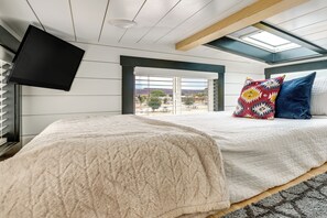 A bedroom with a bed, a television, a skylight, and a view of the outdoors.