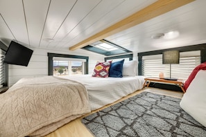 Un dormitorio con cama, mesita de noche, lámpara, televisor y tragaluz.