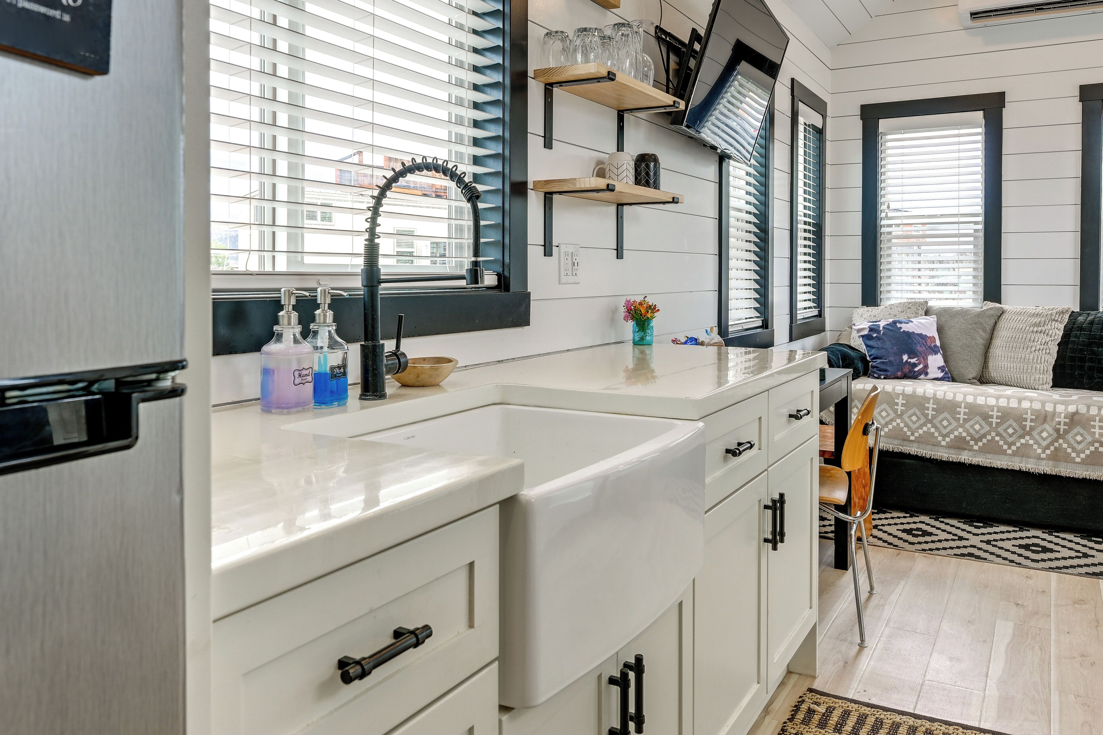 A compact kitchenette with a sink, storage cabinets, and a window with blinds.