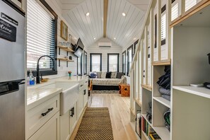 A compact kitchen with a built-in sink, a dining area with a bench, and a bookshelf filled with books. - Gateway to Red Rock Adventures! Resort Tiny Home (Hurricane)